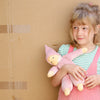 Child holding a pink plush toy against a cardboard box background